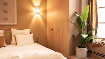 A neatly made bed with white linens and a potted plant beside it.