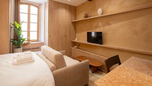 A hotel room with a bed, a sofa, a TV on a shelf, and a small table. - Charming Studio With A/C - 2P - Center St Tropez (Saint-Tropez)