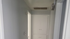 Un pasillo estrecho con suelo de madera y paredes blancas, que conduce a un par de puertas al final.