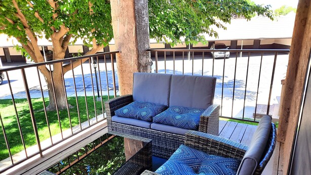 Un balcón con muebles de mimbre, incluyendo un sofá y dos sillones, y vistas a un aparcamiento.