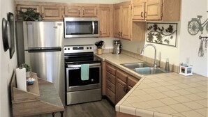 Una cocina con armarios de madera, electrodomésticos de acero inoxidable, microondas, cafetera y pileta.