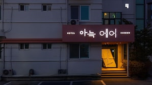 Entrada de hotel com placa em coreano, aparelhos de ar condicionado e sinalização de estacionamento.