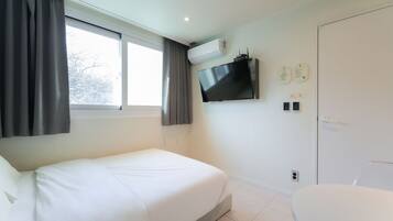 A modern hotel room with a bed, a TV mounted on the wall, and a door with a handle.