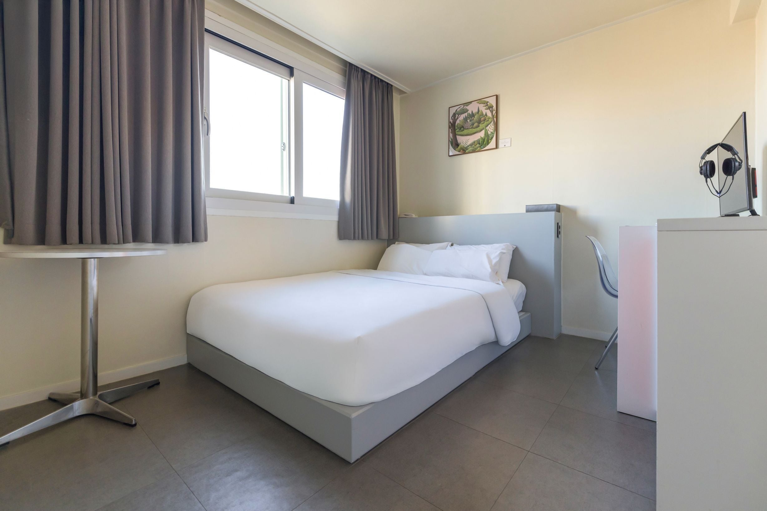 Una habitación de hotel moderna con una cama individual, un escritorio, una silla y un ventanal con cortinas.