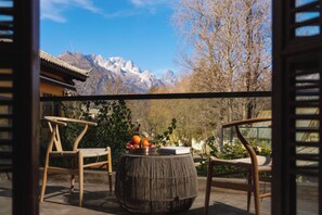 A traditional wooden chair and table set on a balcony with a view of mountains and a clear sky.
