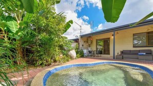 A backyard with a swimming pool, a patio area, and a house with a sliding door and a sofa.