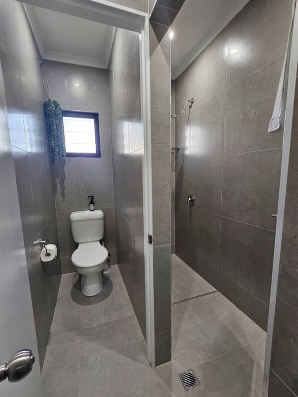A modern bathroom with a toilet, a shower, and a window.