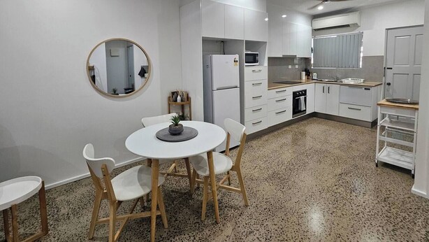 A modern kitchen with white cabinets, a round mirror, and a dining area with a white table and chairs.
