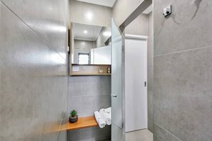 Um banheiro moderno com azulejos cinzas, uma prateleira de madeira com uma planta em vaso e uma toalha branca.