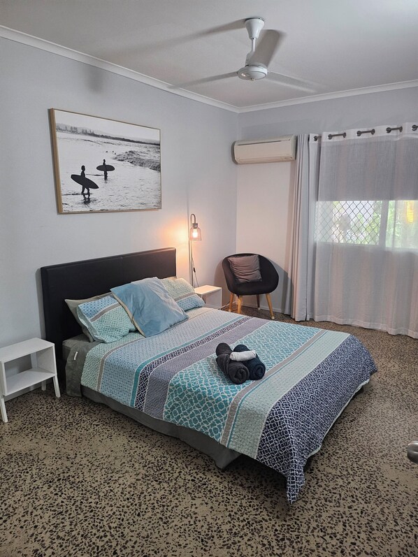 A bedroom with a bed, a chair, a bedside table, a ceiling fan, an air conditioning unit, a window with curtains, and a wall-mounted picture. - Renovated Unit + Private Pool! (Malak)