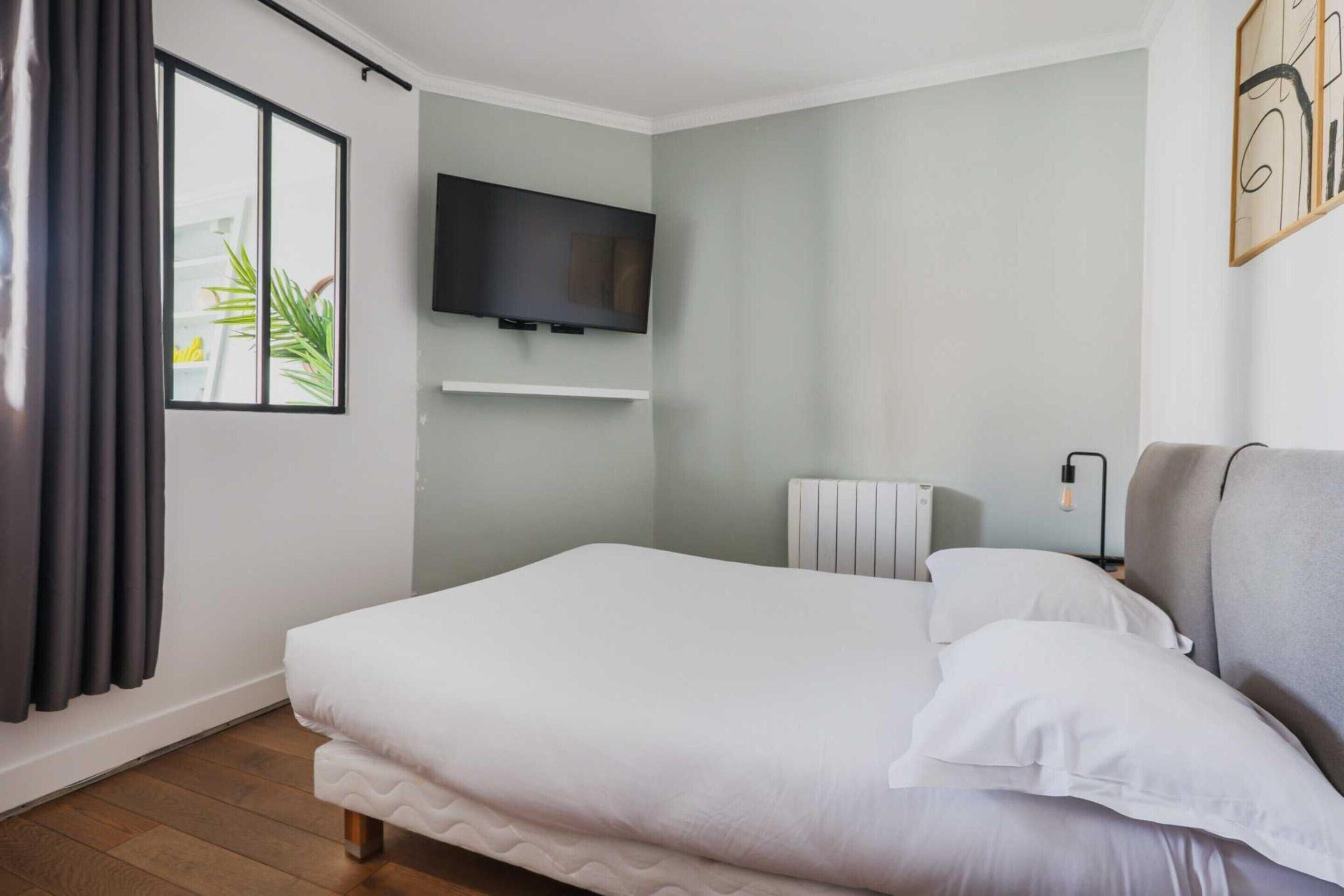 A neatly arranged bedroom with a bed, a television mounted on the wall, and a radiator.