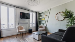 A modern living room with a flat-screen TV, two armchairs, a coffee table, and a bookshelf. - Serene Apartment - 1br/4p - Place de la Bastille (Paris)