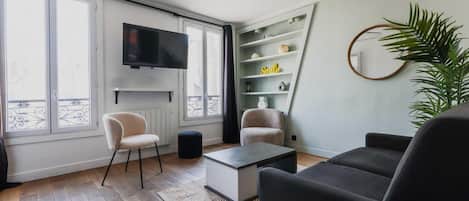 Una sala de estar moderna con un televisor de pantalla plana, dos sillones, una mesa de centro y una estantería.