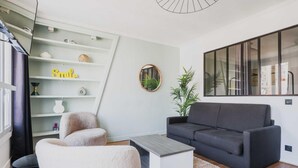 A modern living room with a grey sofa, a white armchair, and a coffee table. There is a bookshelf with decorative items and a mirror on the wall. - Serene Apartment - 1br/4p - Place de la Bastille (Paris)