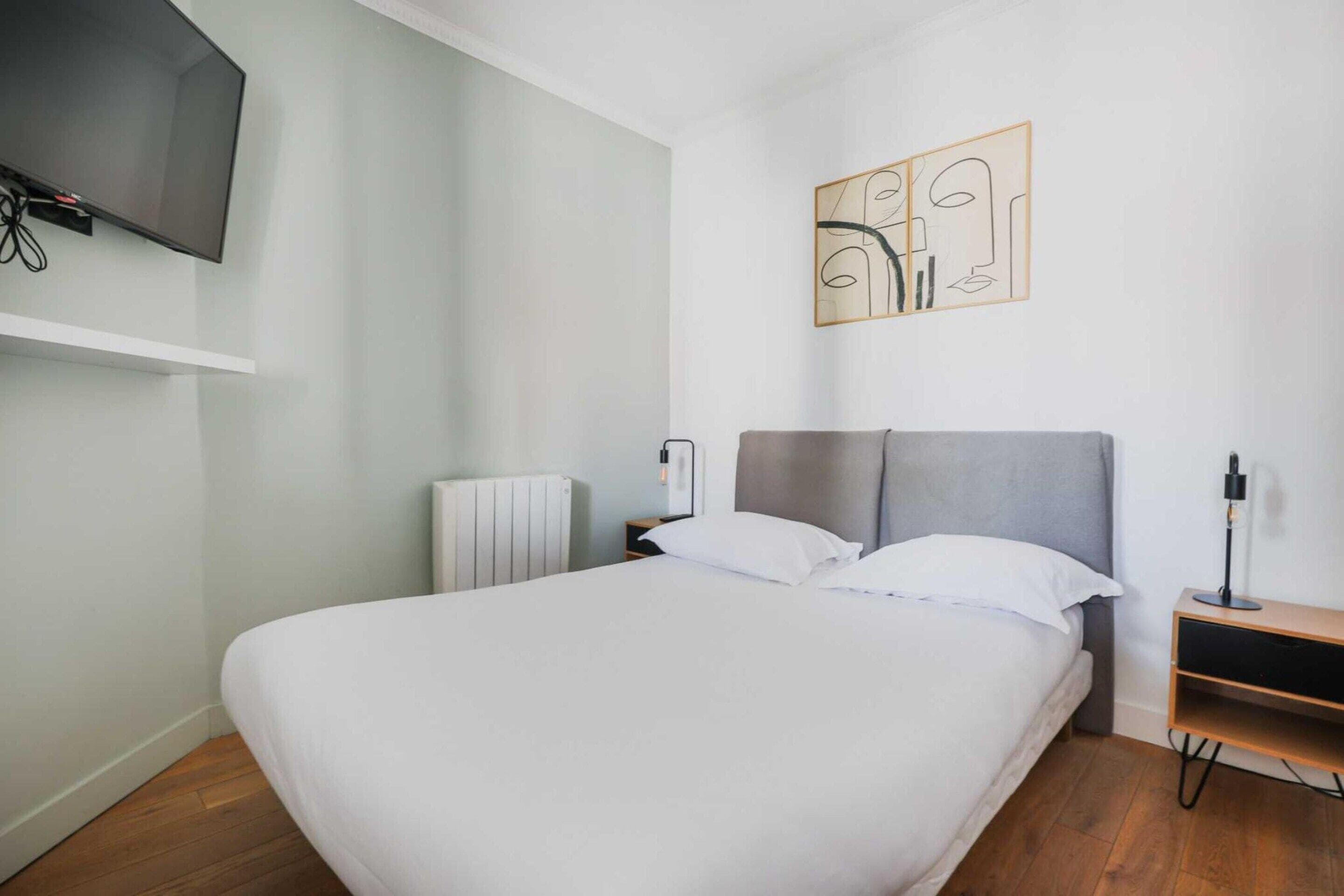 A neatly arranged bedroom with a bed, a bedside table, a lamp, and a wall-mounted TV.