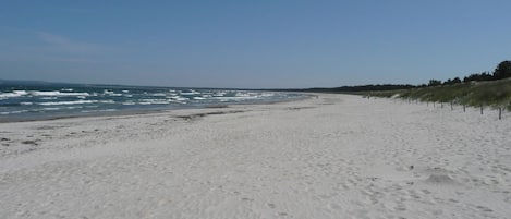 A wide sandy beach with footprints, a clear sky, and a distant shoreline.