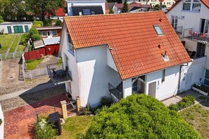 A two-story building with a red-tiled roof, a balcony, and a small garden area. - Haus Windland - 1-room vacation apartment near the harbor with a small garden - House (Wiek)