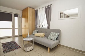 A modern living room with a grey sofa, a small round table, a colorful rug, and a wooden wardrobe. - Haus Windland - 1-room vacation apartment near the harbor with a small garden - House (Wiek)