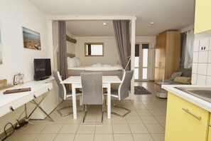 A compact hotel room with a bed, a desk, a chair, a TV, and a kitchenette. - Haus Windland - 1-room vacation apartment near the harbor with a small garden - House (Wiek)