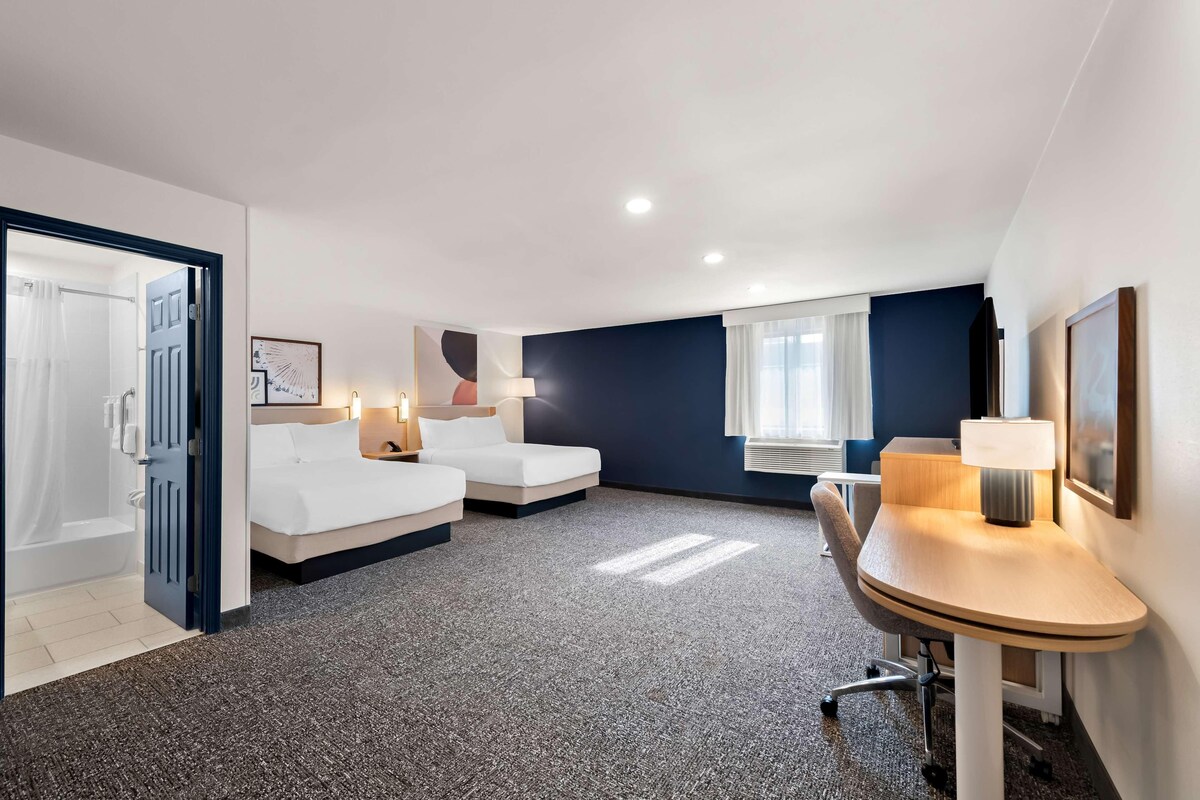 A hotel room with two beds, a desk, a chair, a lamp, and a window.
