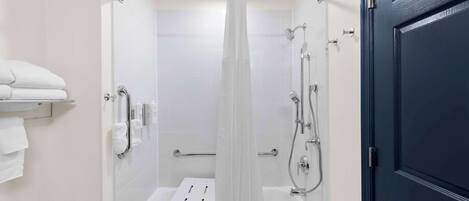 Une salle de bain moderne avec une douche à l’italienne, des carreaux blancs, une paroi de douche en verre et un porte-serviettes blanc.