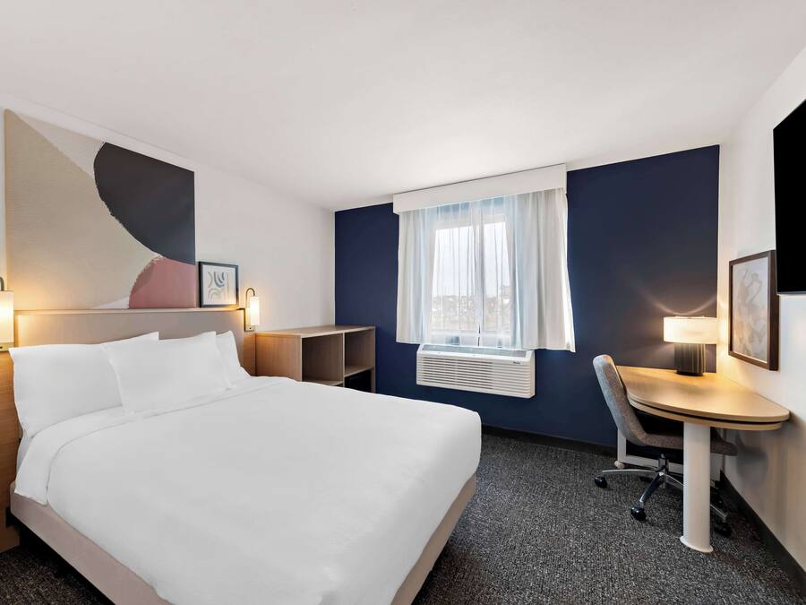 A hotel room with a bed, bedside tables, a desk, and a chair.