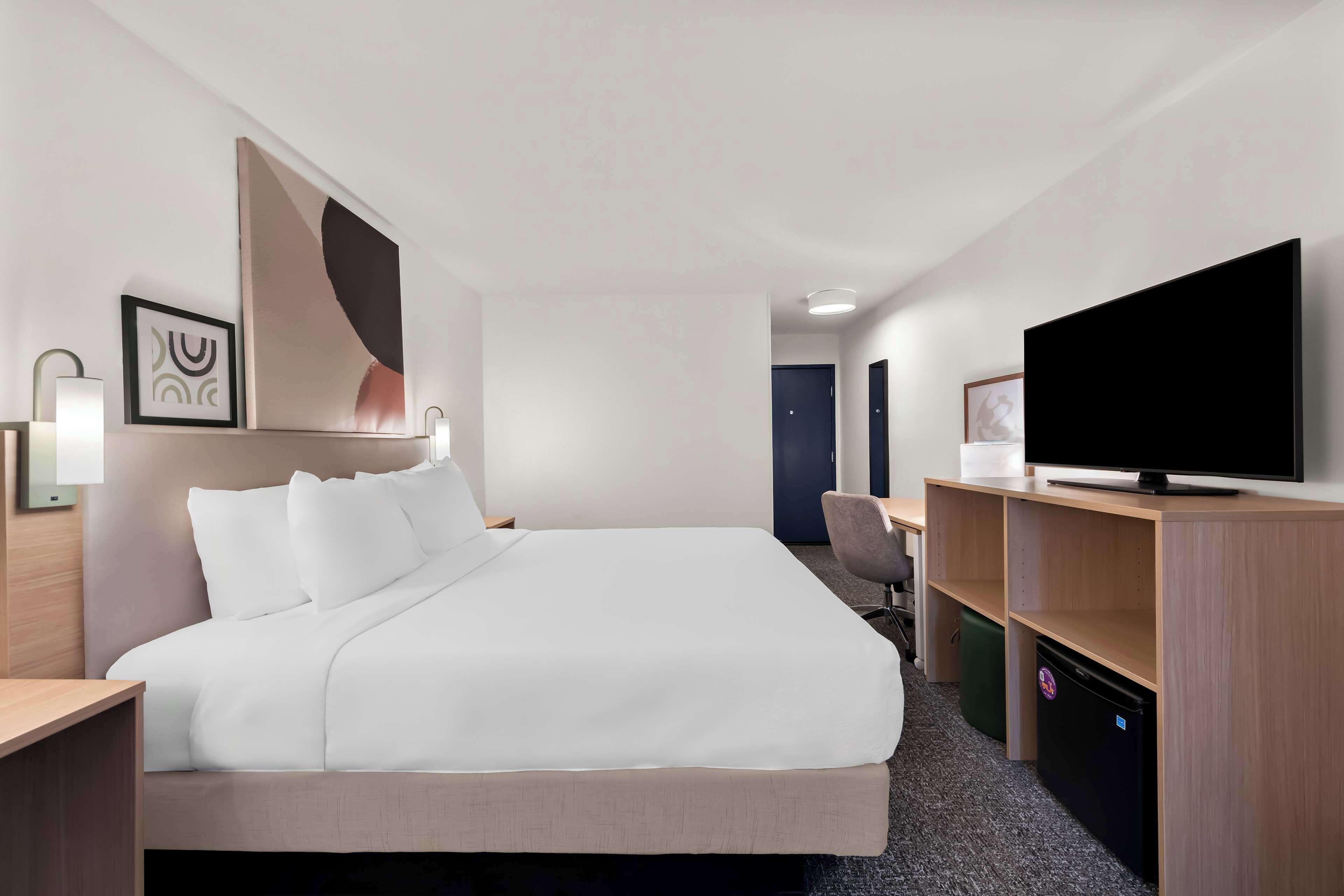 A hotel room with a bed, a desk, a chair, a television, and a small refrigerator.