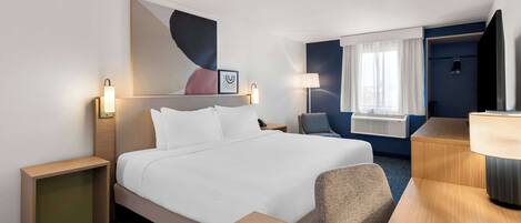 Una habitación de hotel con una cama grande, mesitas de noche, un escritorio, una silla, un televisor y una ventana con cortinas.