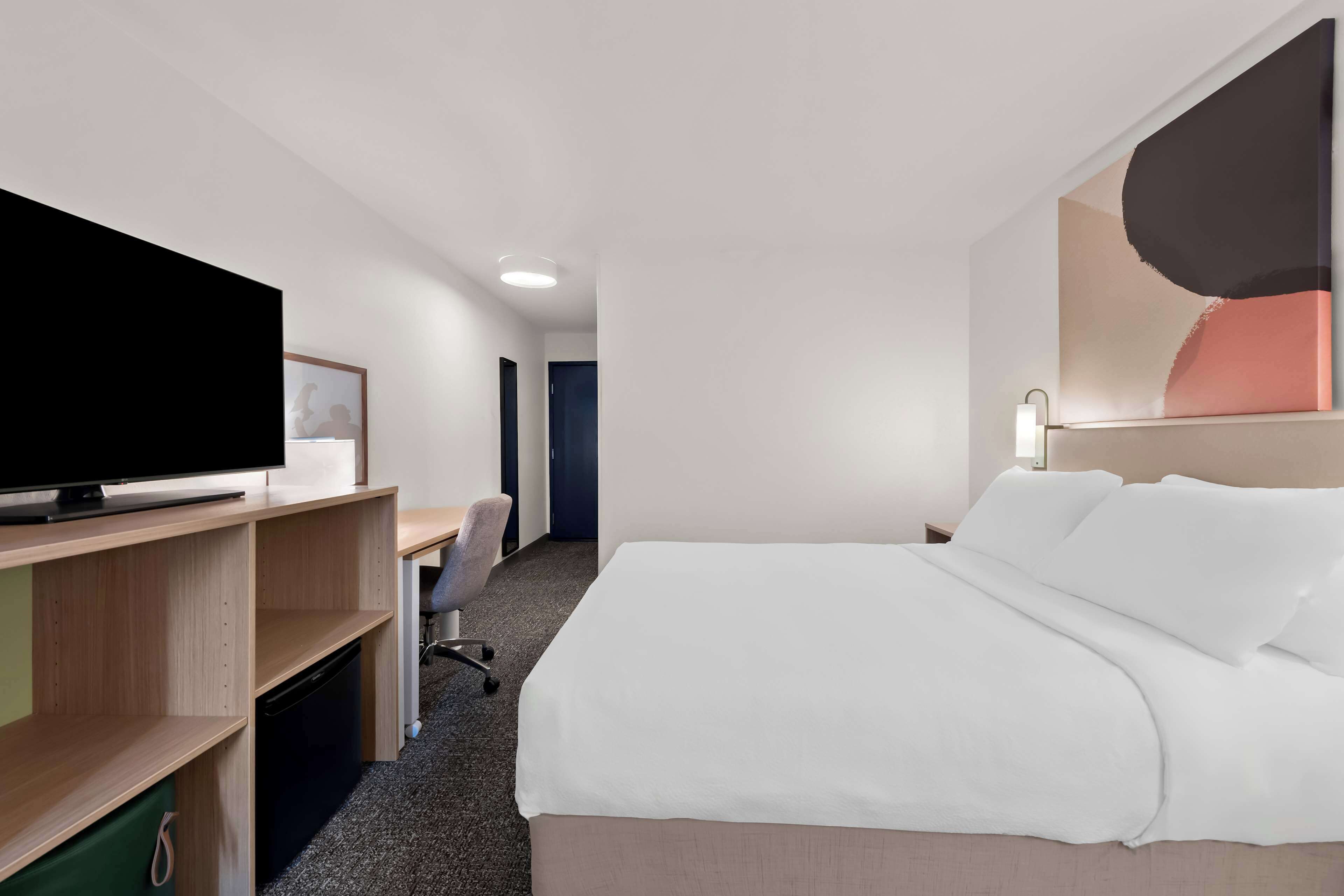 Habitación de hotel con cama, escritorio con silla, televisión y una obra de arte colgada en la pared.