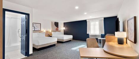 A hotel room with two beds, a desk, a chair, a lamp, and a window with curtains.