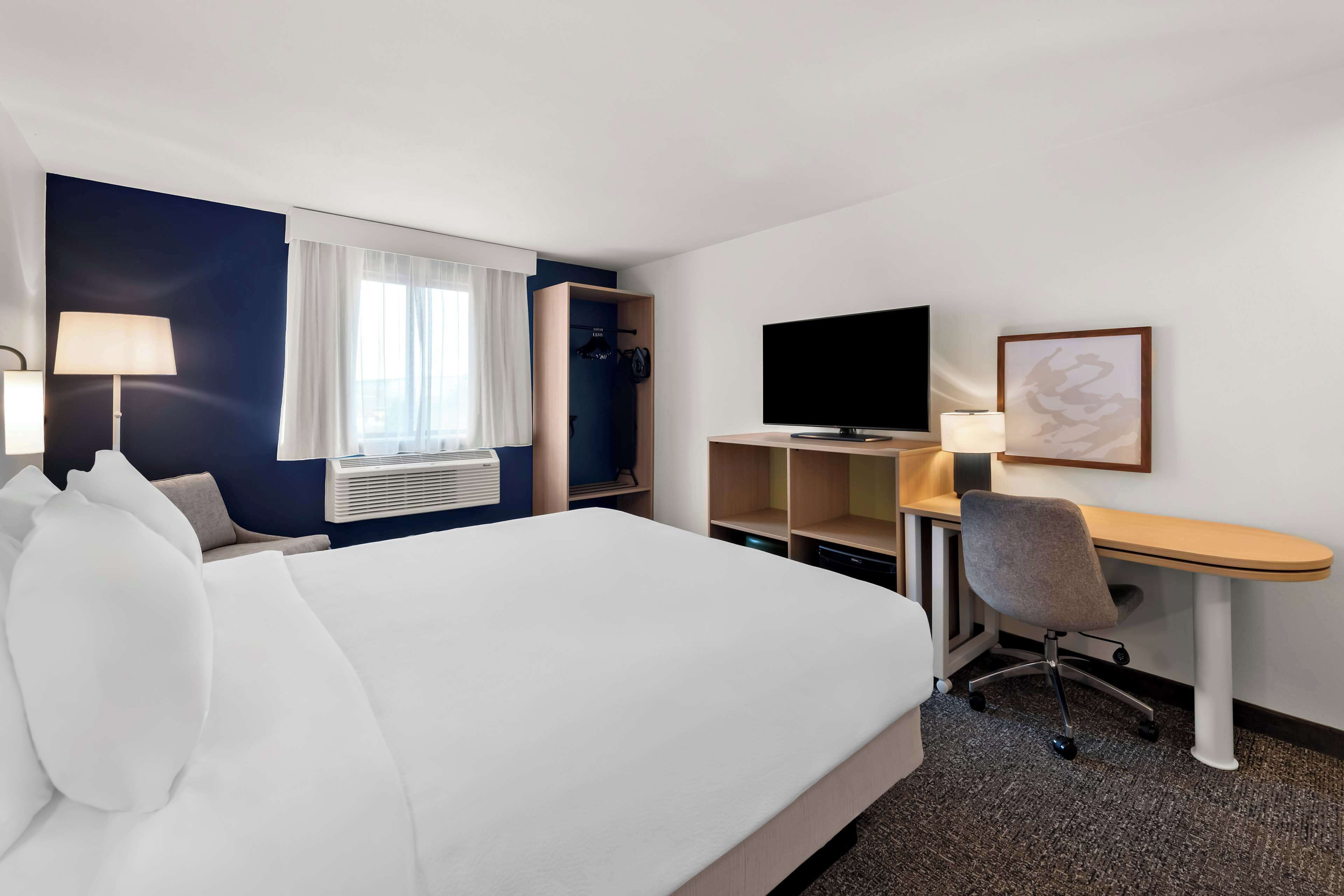 A hotel room with a bed, a desk, a television, and a window with curtains.