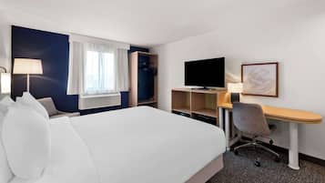 Hotellihuone, jossa on sänky, työpöytä, televisio ja ikkuna, jossa on verhot.