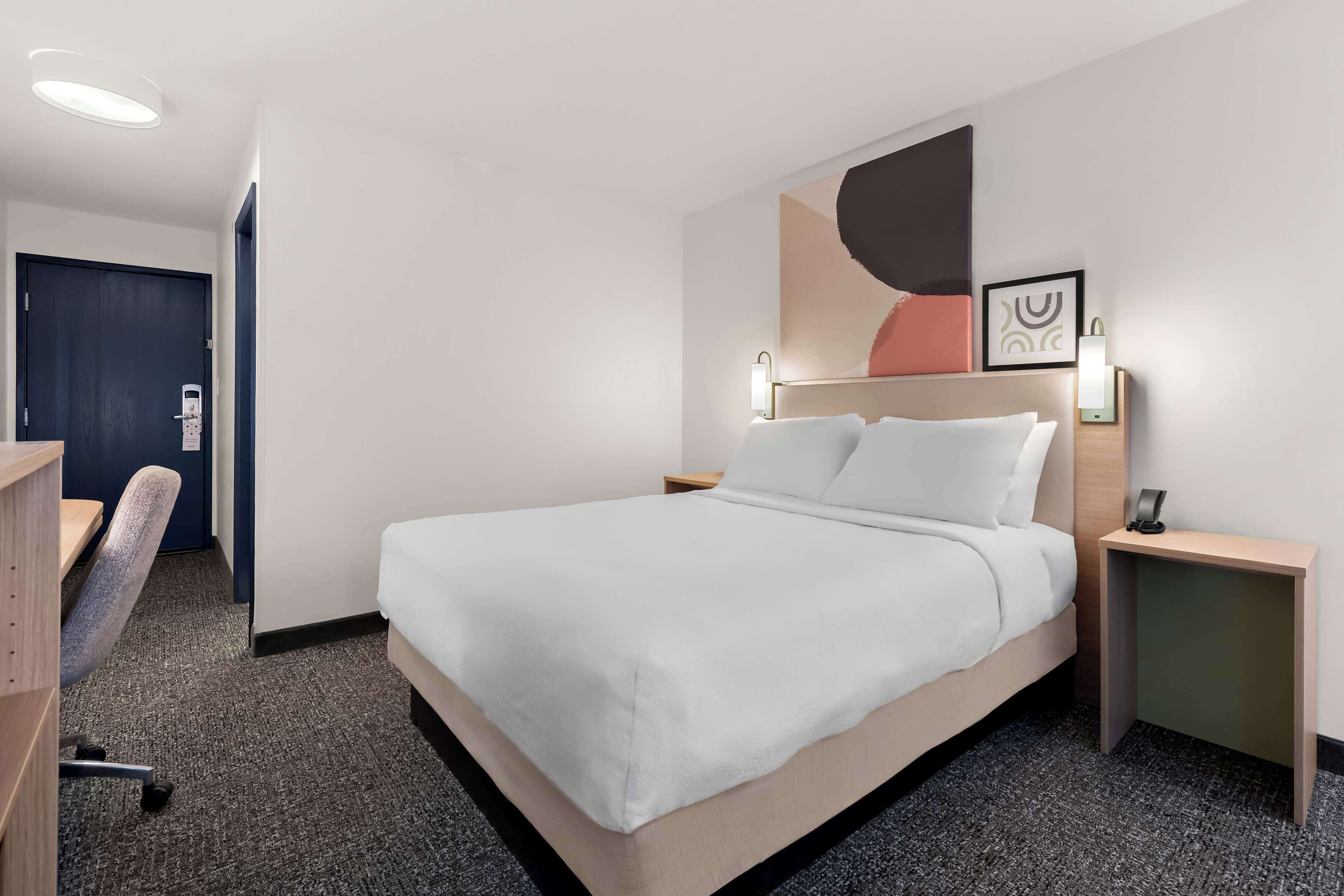 A hotel room with a large bed, a desk, a chair, and a desk lamp.