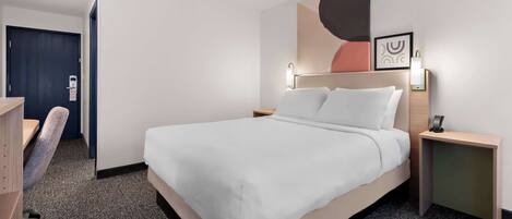 A hotel room with a large bed, a desk, a chair, and a desk lamp.