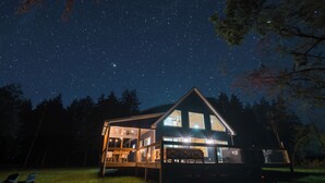 A house with a large deck and multiple windows, surrounded by trees under a starry night sky. - Stunning Home Near Nolin Lake: Hot Tub + Fire Pit! (Cub Run)
