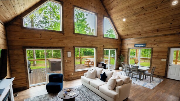 A spacious living room with a high ceiling and large windows, a sofa, a coffee table, and a dining area with a table and chairs. - Stunning Home Near Nolin Lake: Hot Tub + Fire Pit! (Cub Run)