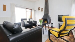Ein Wohnzimmer mit Kamin in Schwarz, gelb-schwarzen Sesseln, einem schwarzen Sofa und einem Fernseher.