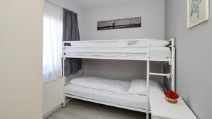 Ein Schlafraum mit Etagenbetten, einem Heizkörper, einem Fenster mit Vorhängen und einem gerahmten Bild an der Wand.