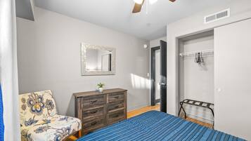 Une chambre à coucher comprenant un lit, une commode, une chaise, un miroir et un ventilateur de plafond.