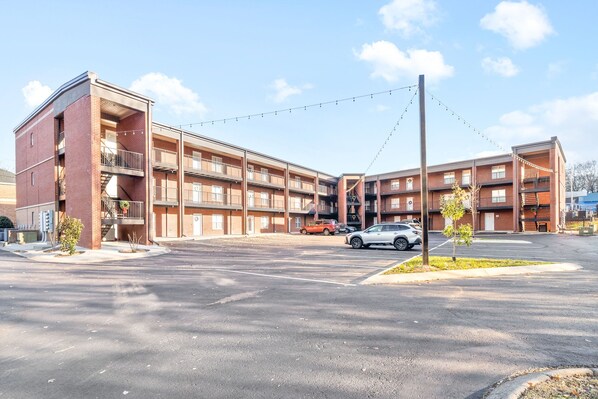 Un edificio de varios pisos de ladrillo con un patio central, zona de estacionamiento y varios coches aparcados.
