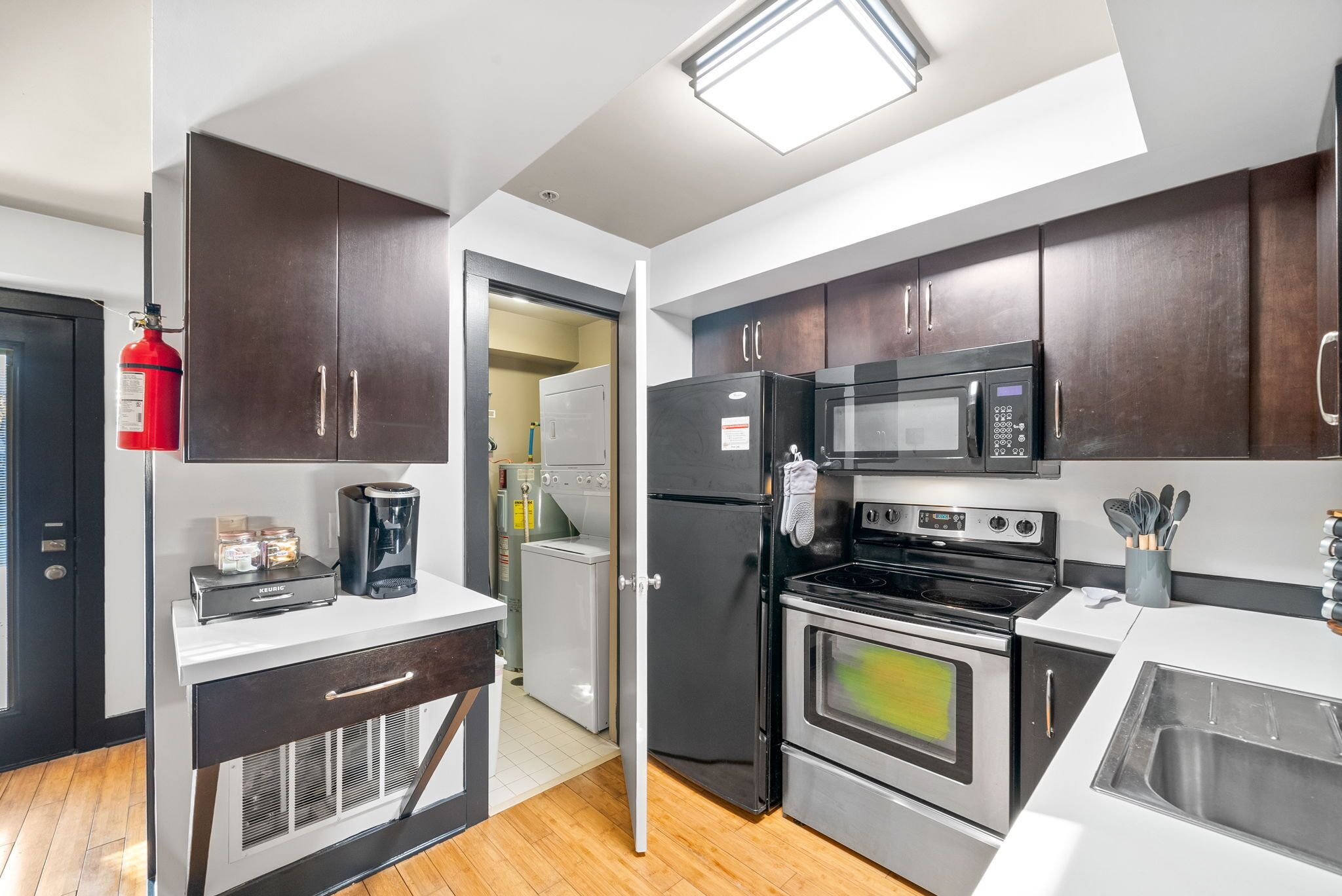 A modern kitchen with dark wooden cabinets, stainless steel appliances, a coffee maker, and a fire extinguisher.