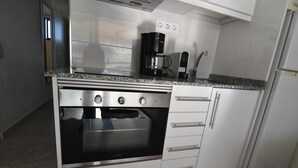 A compact kitchen with a built-in oven, a coffee maker, and a refrigerator. - Discover Costa Brava! Rent this cozy studio in Roses with a pool, close to the beach. Book now! (Roses)