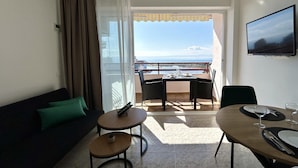 A hotel room with a balcony, a sofa, a dining table set for two, and a TV mounted on the wall. - Discover Costa Brava! Rent this cozy studio in Roses with a pool, close to the beach. Book now! (Roses)