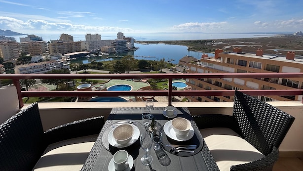 A balcony with a table set for two, overlooking a marina and buildings. - Discover Costa Brava! Rent this cozy studio in Roses with a pool, close to the beach. Book now! (Roses)