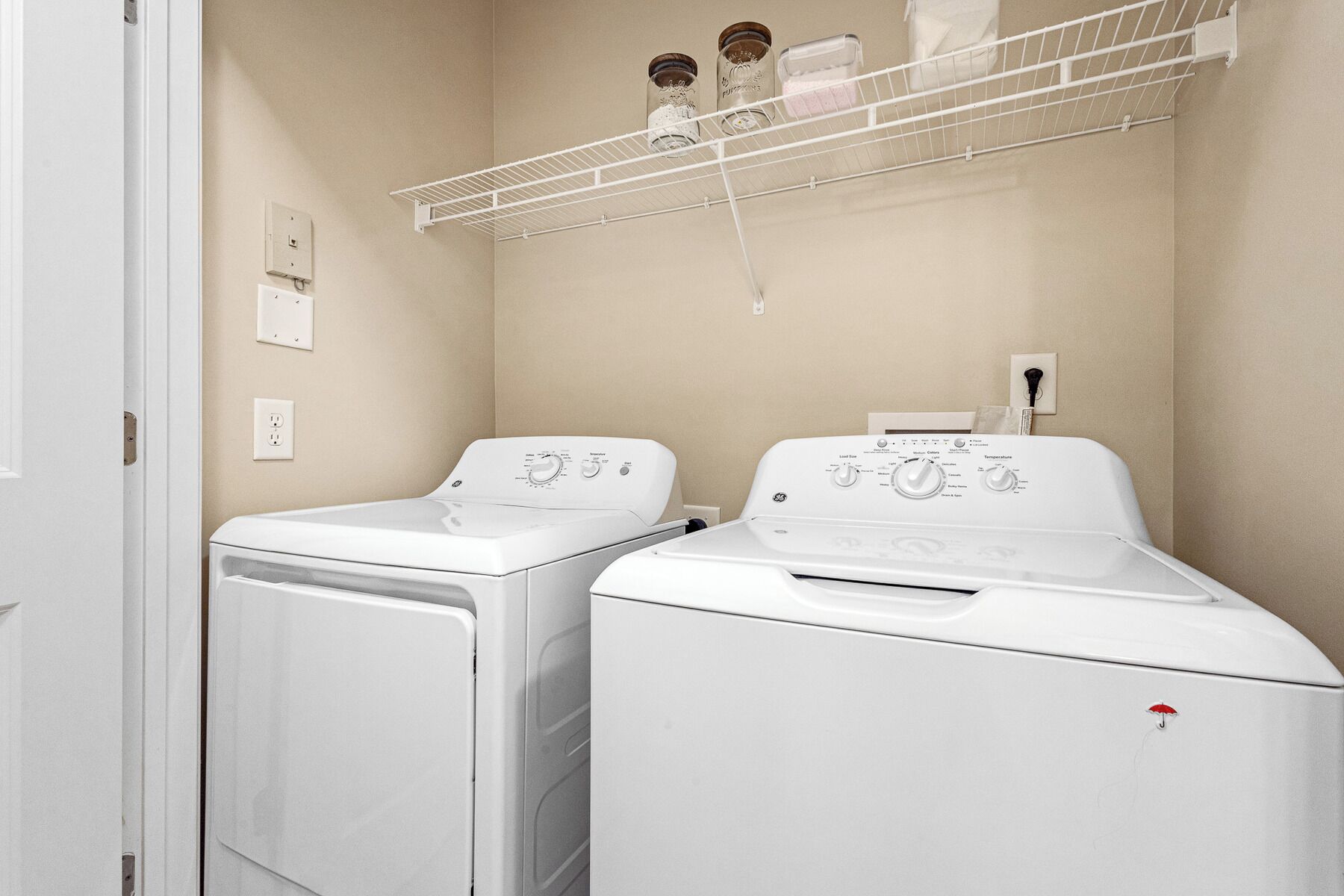 A laundry room with two front-loading washing machines and a drying rack above.