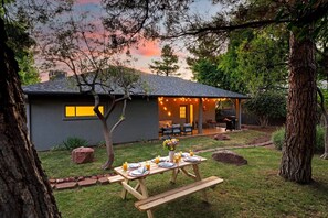 Ein Haus mit einer Terrasse, die zum Essen eingerichtet ist, umgeben von Bäumen und einem Garten.