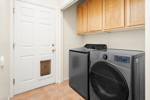 A laundry room with a front-loading washer and dryer, wooden cabinets above, and a white door with a window. - West Sedona Dome, Hot Tub, Red Rock Views, Stargazing, Game room, Pets welcome! (Sedona)
