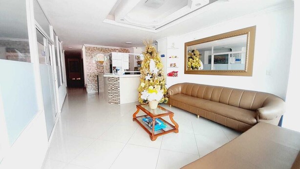 A spacious living room with a brown leather sofa, a wooden coffee table with a vase, and a decorative wall piece. - Hotel Karin (Riohacha)