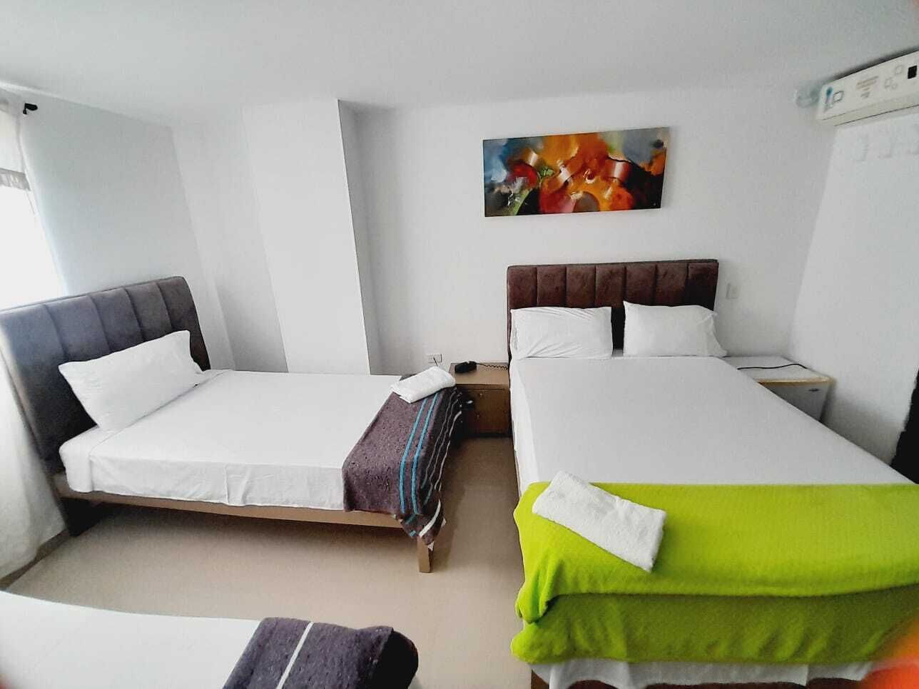 A hotel room with two single beds, a small table, a chair, a nightstand, and a painting on the wall.