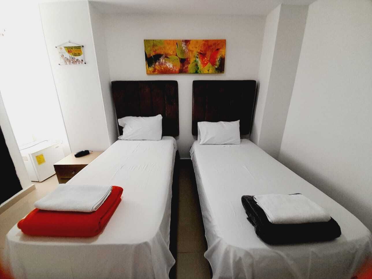 Habitación de hotel con dos camas individuales, ropa de cama blanca y un cuadro abstracto colorido sobre las camas.